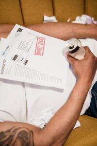 Close up of a Man Lying Down under Unpaid Bills Holding a Bear Can